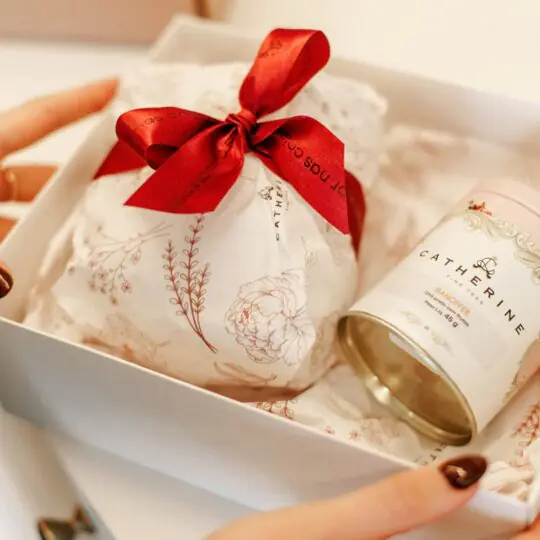 Uma "caixa de afeto" Catherine Fine Teas sendo aberta, revelando a icônica Pink Tin e louças, materializando o ritual sofisticado de presentear com chá.