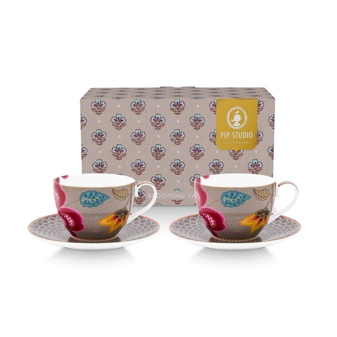 Par de xícaras de chá Pip Studio em porcelana holandesa com pires na cor cáqui, adornadas com grandes flores vibrantes e bordas douradas, exibidas à frente da sua elegante caixa de presente Blooming Tales Pip Studio.